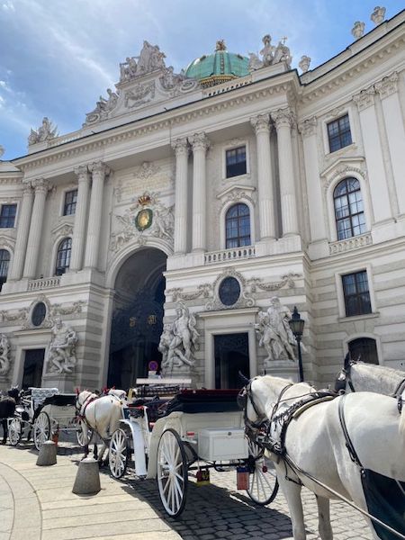 International Pferdekutschen stehen vor einem prächtigen historischen Gebäude mit Skulpturen.